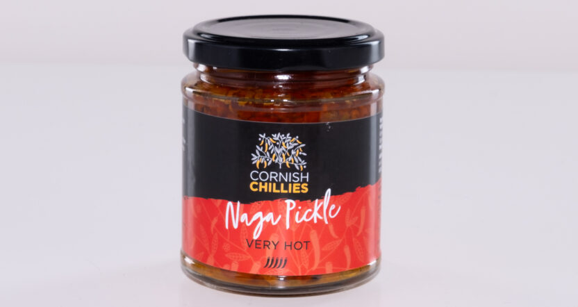 “Glass jar of handmade naga pickle made with UK-grown naga chillies on a rustic kitchen table.”